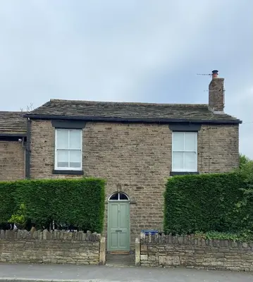 a brick house with a green door and bushes at Old Store Cottage, Up Holland in Upholland
