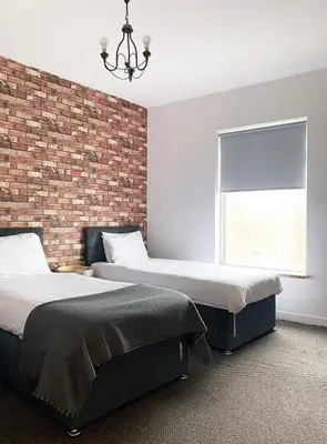 two beds in a room with a brick wall at The Docklands XL by Serviced Living Liverpool in Liverpool