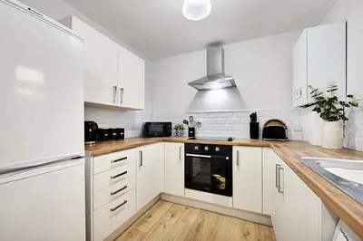 a white kitchen with wooden floors and white cabinets at Balfour House - Air Host & Stay - Sleeps 8, free parking in Litherland