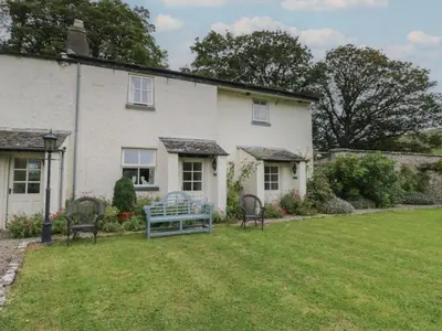 a white house with two chairs in a yard at The Gameskeepers Cottage in Grange Over Sands