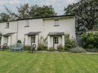 a white house with a bench in the yard at The Gameskeepers Cottage in Grange Over Sands
