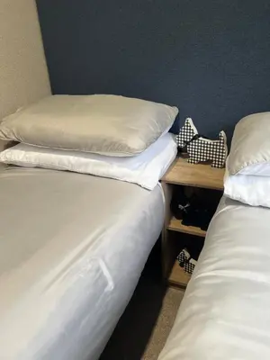 two beds with white sheets and a nightstand between them at Modern Caravan 2025 with Decking in Morecambe