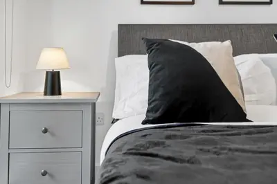 a bed with a black pillow and a nightstand with a lamp at 2BR Apt - City Centre - Parking - Balcony - Long Stays - Contractors in Liverpool
