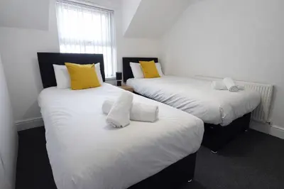 two beds with yellow and white pillows in a room at The Big Home - 8 bedrooms, 11 Beds, Long stays welcome, Free parking in Wallasey