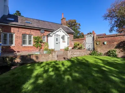 a brick house with a green lawn in front of it at Gardener's Cottage in Lytham St Annes