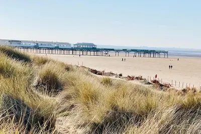 a beach with a pier and people on the sand at Pier View in Lytham St Annes