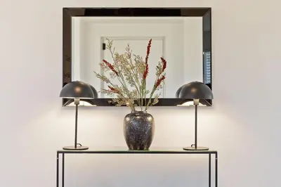 a vase on a table with two lamps and a mirror at Fellbeck Holiday Home - Cartmel in the Lake District in Cartmel