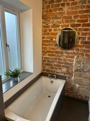 a large white bath tub in a bathroom with a brick wall at Cosy Apartment in Wallasey Village Near Liverpool in Wallasey