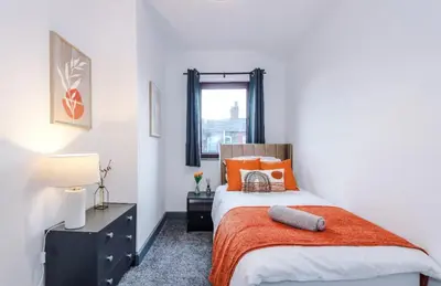 a bedroom with a bed with an orange blanket and a window at Three Bedroom House in Wigan - Perfect for family! in Ince-in-Makerfield