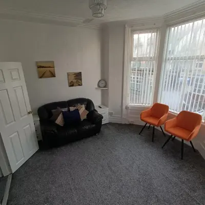 a living room with a black leather couch and two orange chairs at Jubilee holiday flats in Blackpool