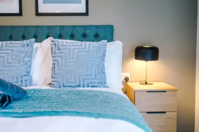 a bedroom with a bed with a blue headboard and a lamp at High End 2BR 2BA Parking City Access in Liverpool