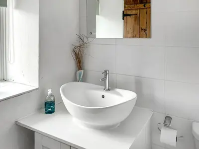 a white bathroom with a sink and a mirror at Oronsay Cottage in Ulverston