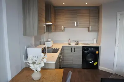 a kitchen with wooden cabinets and a table with a washing machine at Melbourne House Gem Stylish 2-Bed in City Centre in Accrington