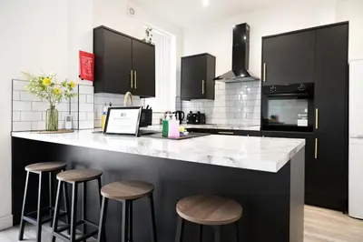 a kitchen with black cabinets and a counter with stools at Antrim House by Serviced Living Liverpool in Liverpool