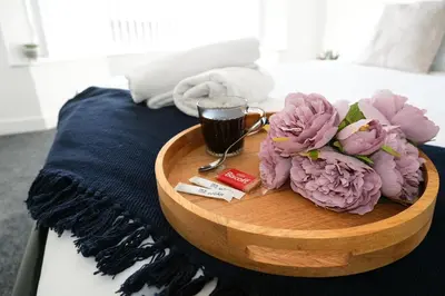 a wooden tray with flowers and a cup of coffee on a bed at Antrim House by Serviced Living Liverpool in Liverpool