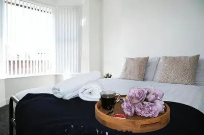 a bed with a tray with a drink and flowers on it at Antrim House by Serviced Living Liverpool in Liverpool