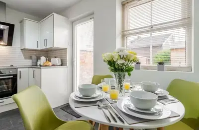 a white kitchen with a table with a vase of flowers at Ribby Stays - 2 bed Cottage Pet Friendly in Wrea Green