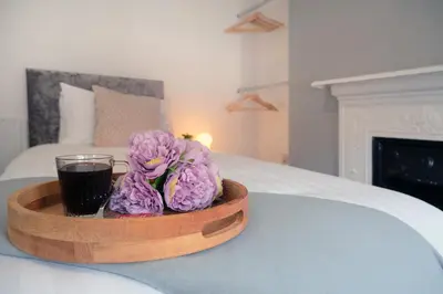 a tray with a drink and purple flowers on a bed at Whitland House by Serviced Living Liverpool in Liverpool