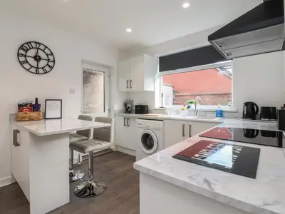 a kitchen with white cabinets and a clock on the wall at Beach Side Bungalow in Lytham St Annes