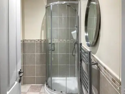 a shower with a glass door and a mirror at Paddy's Cottage in Flookburgh