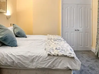 a white bed with blue pillows in a room at Paddy's Cottage in Flookburgh