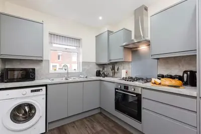 a kitchen with white cabinets and a washer and dryer at Norris Stays - Sleeps 7 by M55 in Preston