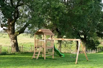 a wooden playground with a slide and a tree at Kidsnape Farm by Wigwam Holidays in Goosnargh