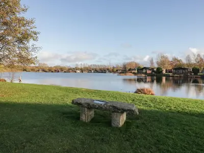 a stone bench sitting in the grass next to a lake at Bluebell Lodge in Carnforth