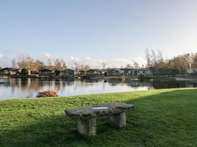 a stone bench sitting in the grass next to a lake at Bluebell Lodge in Carnforth