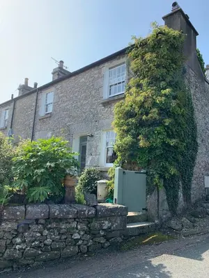 a stone house with a stone wall and a tree at Rock Cottage - Log burners and jacuzzi bath in Lindale