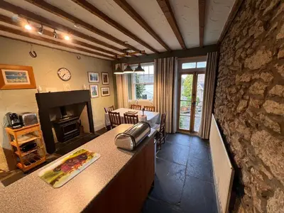 a kitchen with a stone wall and a living room at Rock Cottage - Log burners and jacuzzi bath in Lindale