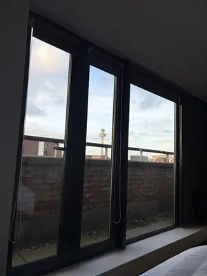 three windows in a bedroom with a view of a brick wall at Liverpool City Centre - Skyline Apartment in Liverpool