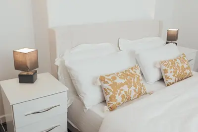 a white bed with pillows and a nightstand with two lamps at Stylish 3 Bed Home with 4 beds- 5 Min walk From Anfield Stadium in Liverpool