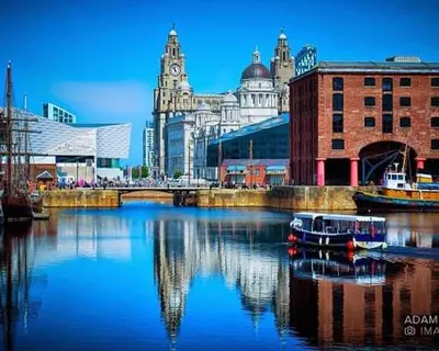 a river with buildings and a boat in the water at Sarah's Woodland Liverpool Stays in Waterloo