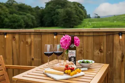 a wooden table with two glasses of wine and food at Hidden Hills Luxury Glamping in Arkholme