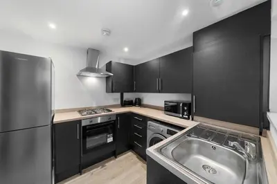 a kitchen with black cabinets and a stainless steel sink at Bibbys in Litherland