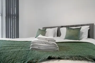 a bed with a green blanket and pillows at Bibbys in Litherland