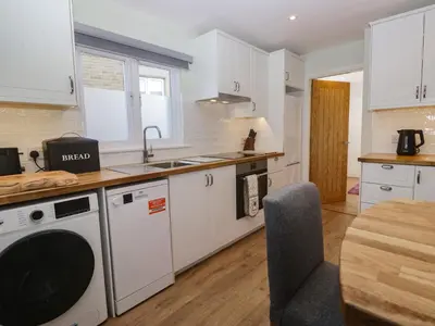 a kitchen with white cabinets and a sink and a table at Drapers Cottage in Grange Over Sands