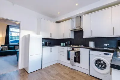 a kitchen with white cabinets and a washer and dryer at Presented by LTJ PrimeKey Properties - NEW! 4 Bed plus Sofa Bed, Perfect for Contractors in Saint Helens