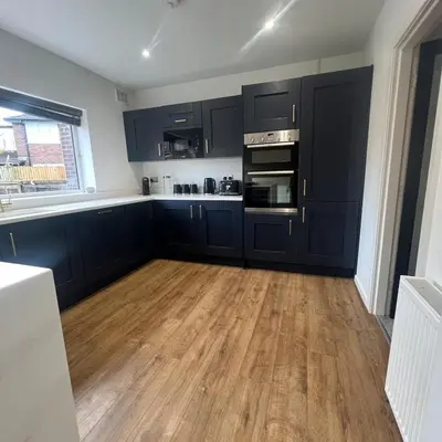 a kitchen with black cabinets and a wooden floor at Stylish family home with cinema-style lounge near Blackpool in Blackpool