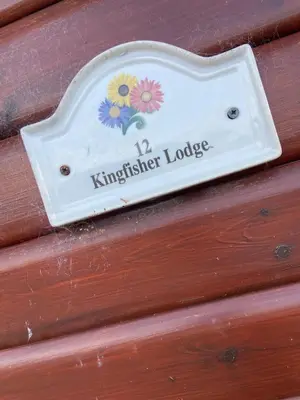 a sign on a wooden wall with flowers on it at Kingfisher Cosy Lakeside Lodge in Carnforth