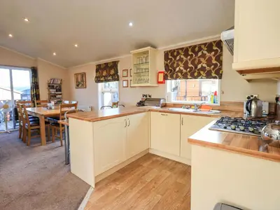a kitchen with white cabinets and a dining room with a table at Kingfisher Lodge - Arnside 14 in Carnforth