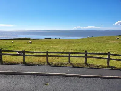 a fence on the side of a road with animals in a field at Retreat By The Seaside in Heysham