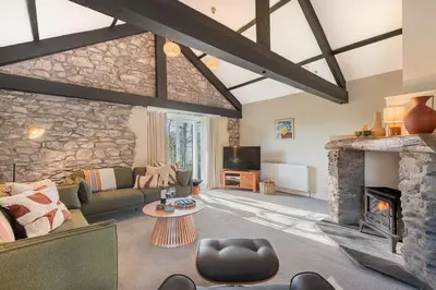 a living room with a fireplace and a stone wall at Royal Oak Barn - Cartmel, Sleeps 8 NEW in Cartmel