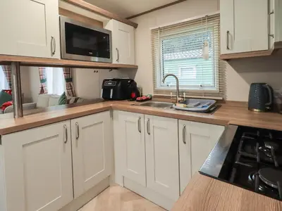 a kitchen with white cabinets and a sink and a microwave at Foxwood Hideaway in Carnforth