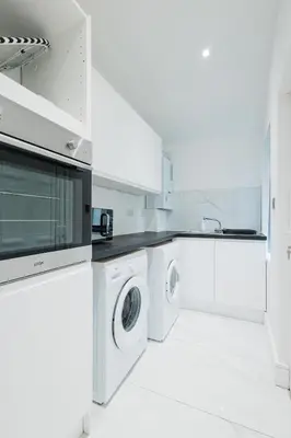 a white kitchen with a washer and dryer at Spacious 4 Bedroom House - Sleeps 10 Guests, Contractors, Groups, Families, Business, Travel, Leisure And Relocation Stays Welcome, 13 Mins From Liverpool City Centre, Fast Wi-Fi, Smart TV In Front Room & FREE Parking, Long Stays And Short Stays Welcome in Liverpool
