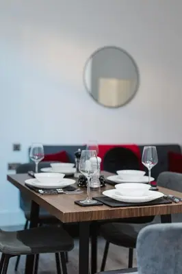 a wooden table with glasses and plates on it at Spacious 4 Bedroom House - Sleeps 10 Guests, Contractors, Groups, Families, Business, Travel, Leisure And Relocation Stays Welcome, 13 Mins From Liverpool City Centre, Fast Wi-Fi, Smart TV In Front Room & FREE Parking, Long Stays And Short Stays Welcome in Liverpool