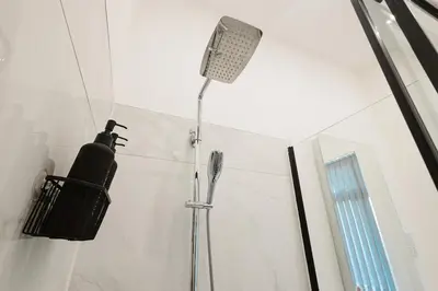 a shower in a white bathroom with a shower head at Spacious 4 Bedroom House - Sleeps 10 Guests, Contractors, Groups, Families, Business, Travel, Leisure And Relocation Stays Welcome, 13 Mins From Liverpool City Centre, Fast Wi-Fi, Smart TV In Front Room & FREE Parking, Long Stays And Short Stays Welcome in Liverpool