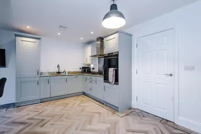 a kitchen with white cabinets and a wooden floor at Driveway Stunning 3Bedroom Home in Preston in Broughton