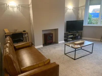a living room with a leather couch and a flat screen tv at Seaside Serenity in Lytham St Annes